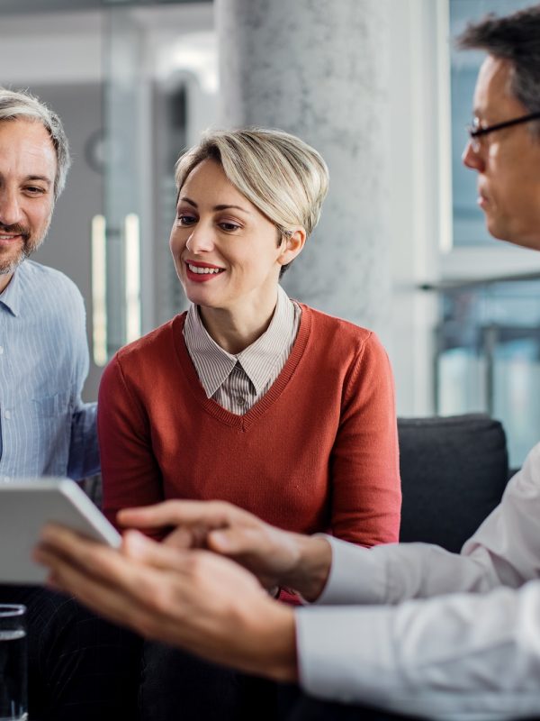 Happy mid adult couple using touchpad with their financial consultant in the office.